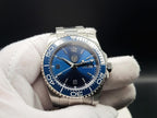 The Memo SJT Original wristwatch with a blue dial and blue bezel, held in a white gloved hand against a dark background.