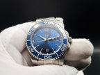 The Memo SJT Original wristwatch with a blue dial and blue bezel, held in a white-gloved hand against a dark background.