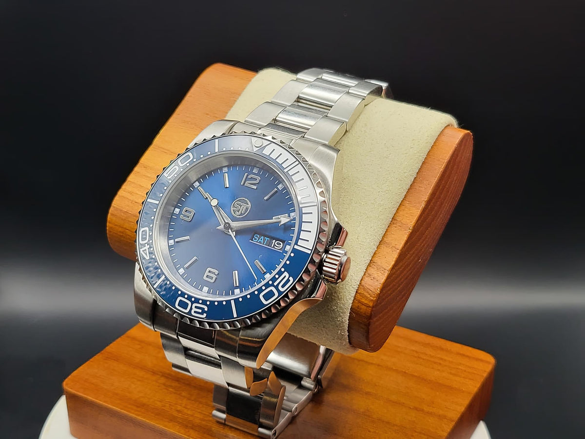 The Memo SJT Original wristwatch with a blue dial and blue bezel, displayed on a wooden stand with a beige cushion against a dark background.