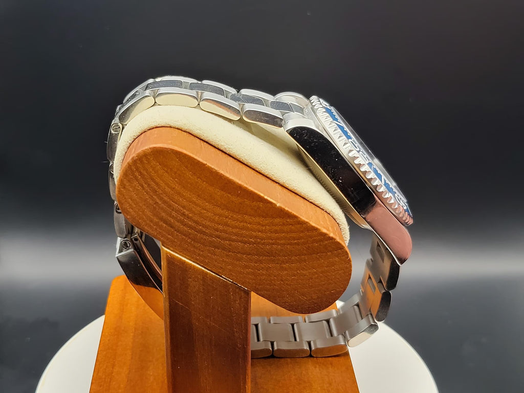 The Memo SJT Original wristwatch with a blue dial and silver bezel, displayed on a wooden stand with a cream cushion against a dark gray background.