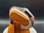 The Memo SJT Original wristwatch with a blue dial and silver bezel, displayed on a wooden stand with a cream cushion against a dark gray background.