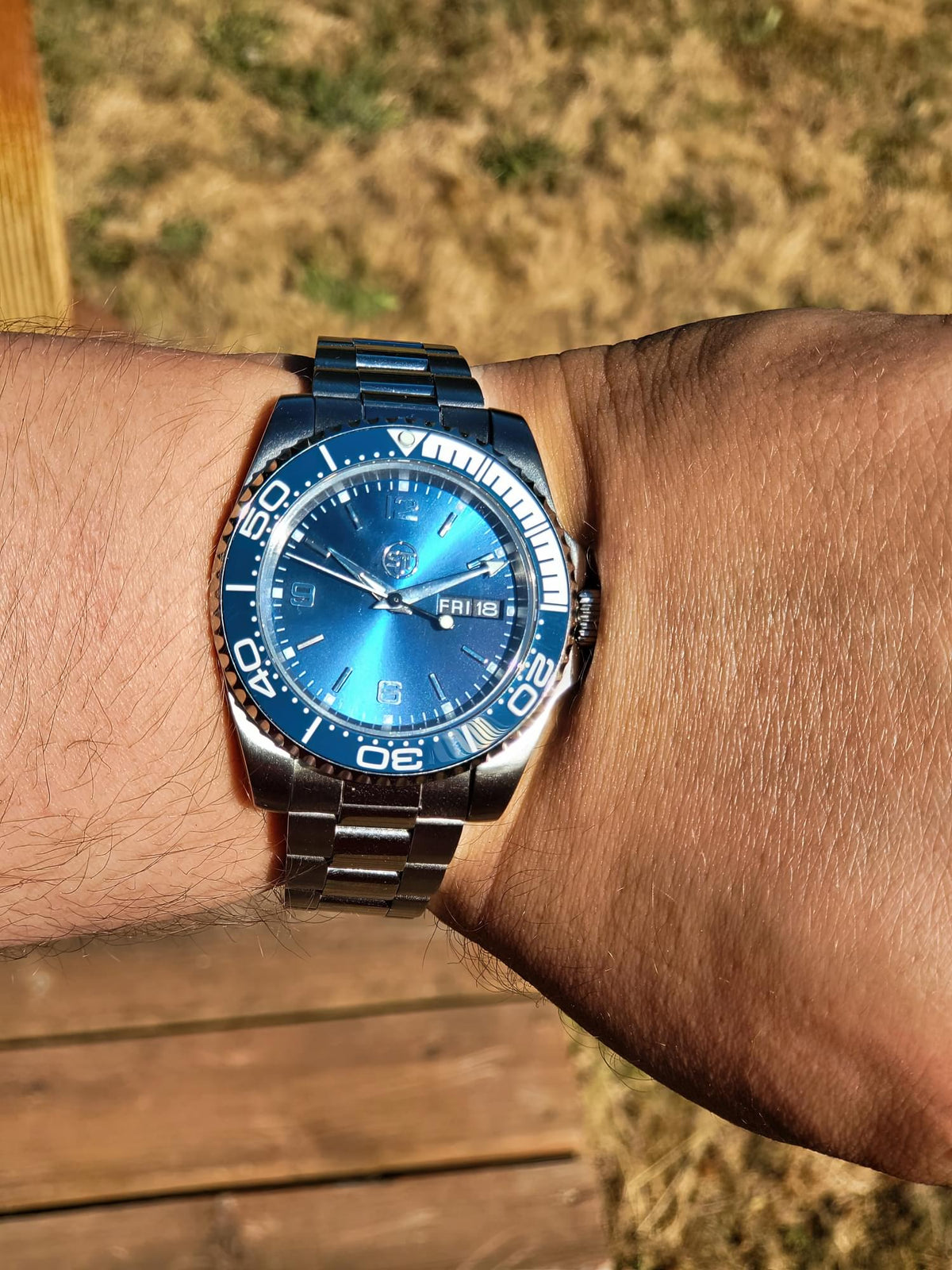 The Memo SJT Original wristwatch with a blue sunburst dial and a silver stainless steel bracelet, worn on a person's wrist outdoors.