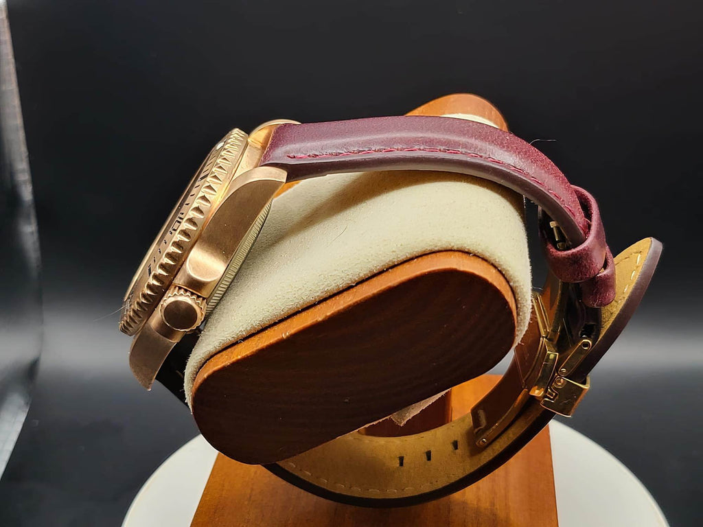 The Midas SJT Original wristwatch with a burgundy leather strap, displayed on a wooden stand with a cream-colored cushion against a dark background.