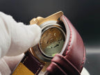 Close-up of The Midas SJT Original wristwatch back with a transparent case cover showing the mechanical movement, held by a white-gloved hand against a dark background.