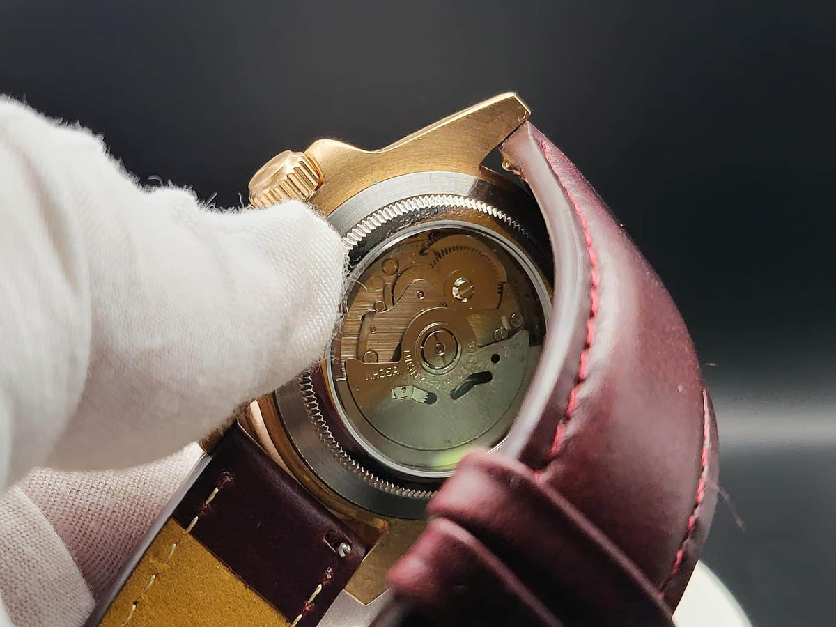 Close-up of The Midas SJT Original wristwatch back with a transparent case cover showing the mechanical movement, held by a white-gloved hand against a dark background.