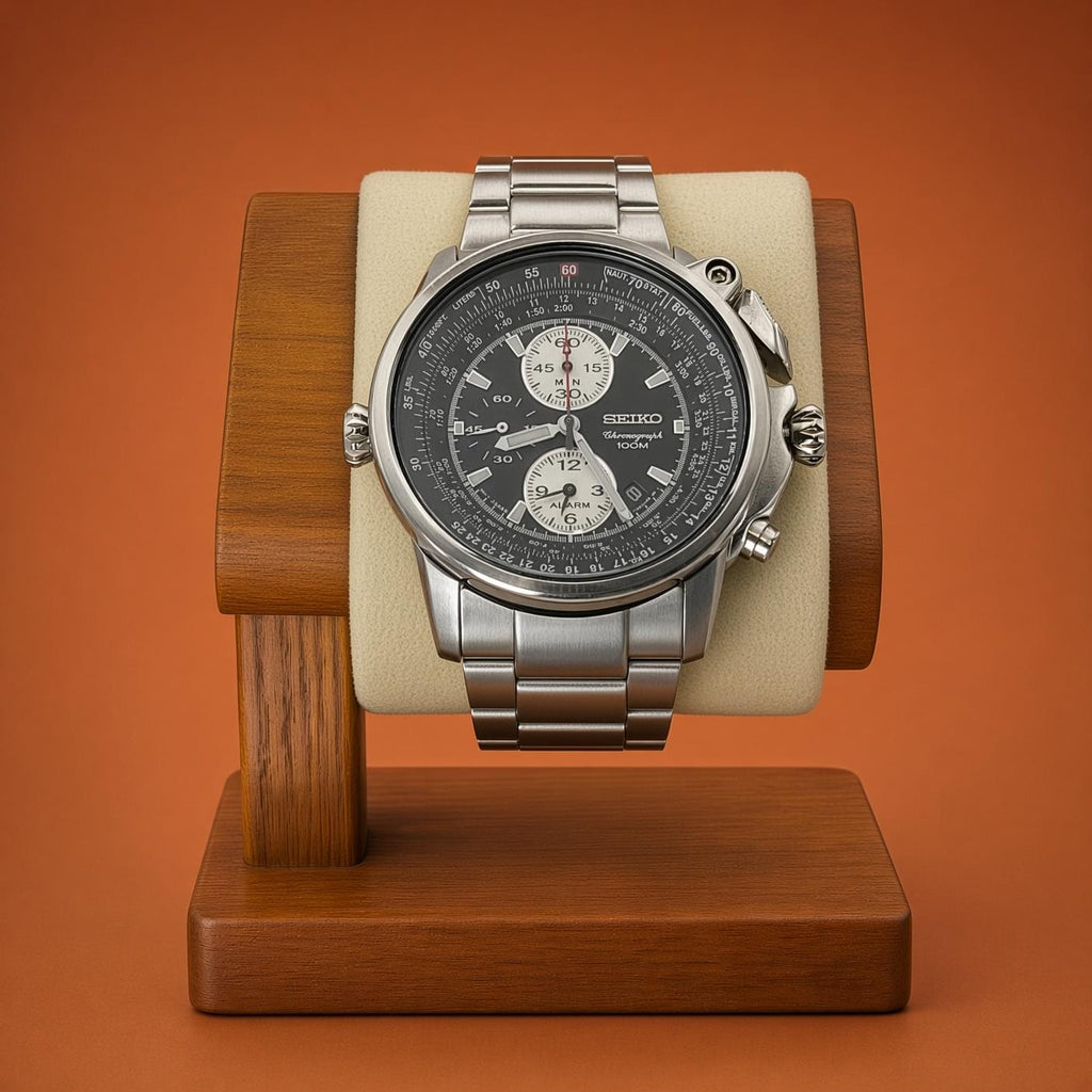 A Seiko Flightmaster stainless steel chronograph watch displayed on a cream cushion mounted in a wooden stand against a solid orange-brown background.