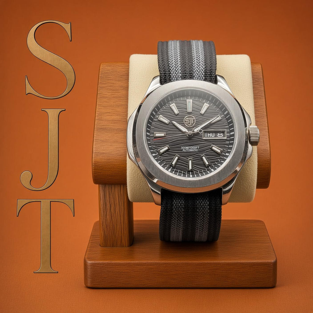 The Alias SJT Original wristwatch with a dark gray sunburst dial, silver-toned case, and black-and-gray textured strap, displayed on a wooden stand against a warm orange-brown background. Large gold letters 'SJT' appear along the left side.