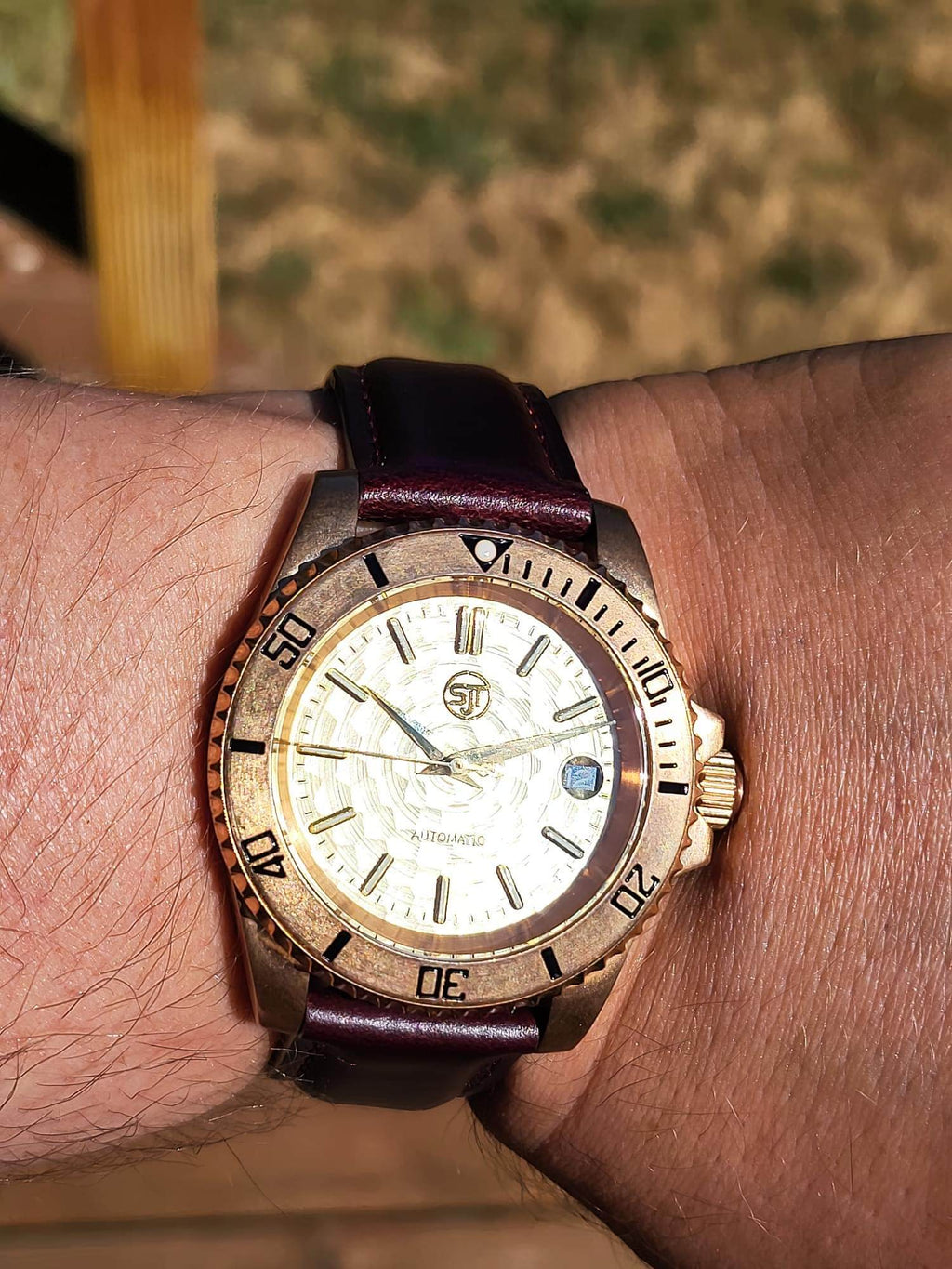 The Midas SJT Original wristwatch with a bronze-toned case, white dial, and dark brown leather strap worn on a person's wrist.