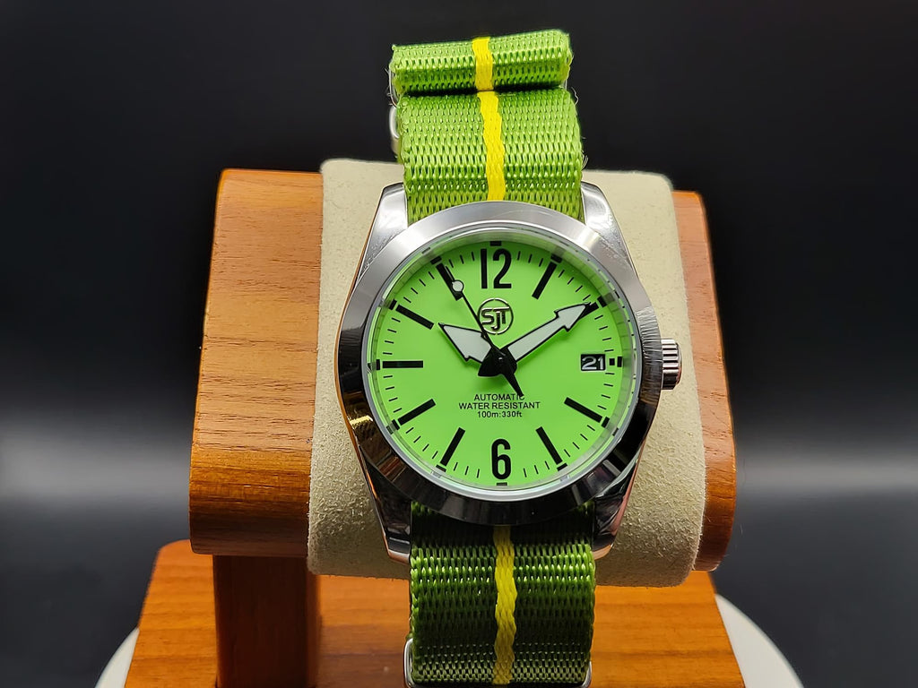 The P-A-R-T-Y? SJT Original wristwatch with a bright green dial, black hands and markers, a silver-tone case, and a green nylon strap with a yellow stripe, displayed on a wooden stand against a dark background.