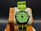 The P-A-R-T-Y? SJT Original wristwatch with a bright green dial, black hands and markers, a silver-tone case, and a green nylon strap with a yellow stripe, displayed on a wooden stand against a dark background.