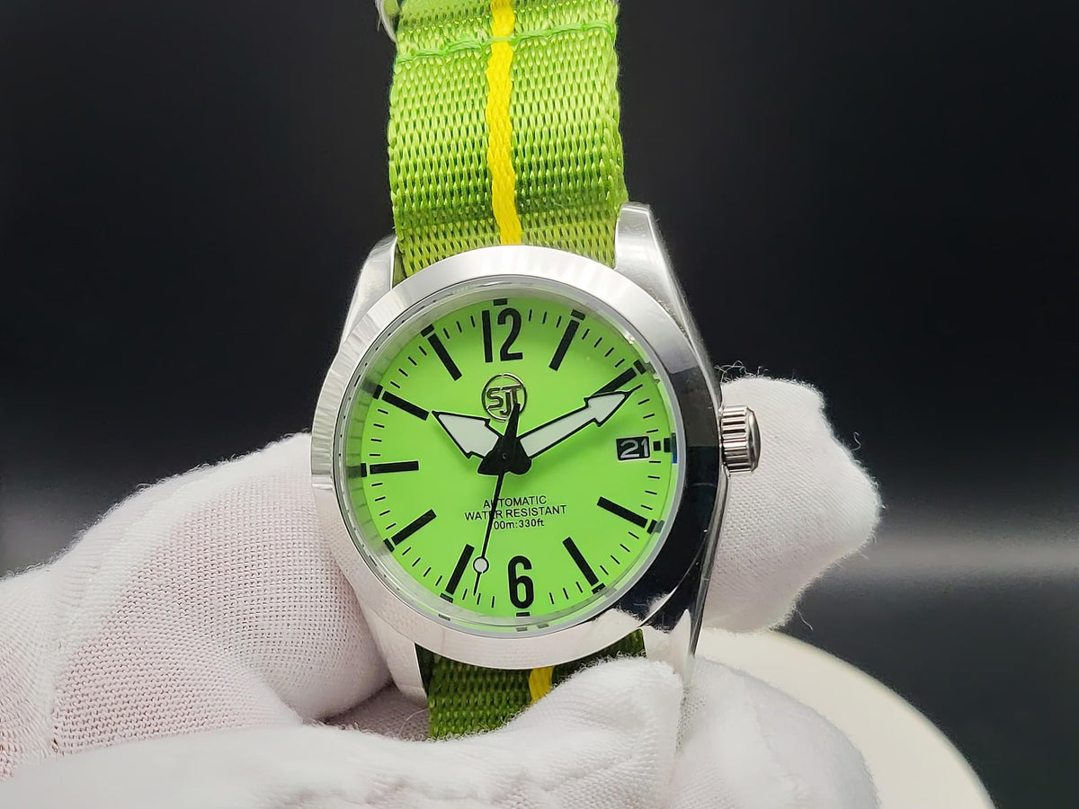 The P-A-R-T-Y? SJT Original wristwatch with a bright green dial and a green fabric strap featuring a yellow stripe, held by a white gloved hand against a dark background.