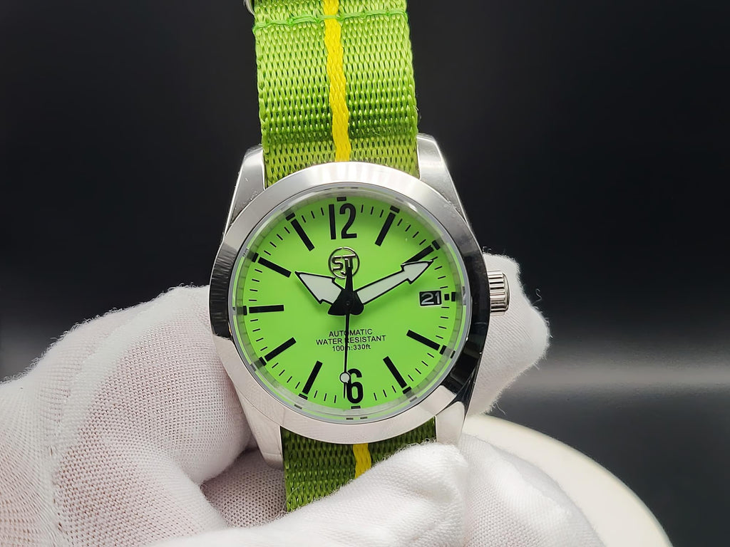 The P-A-R-T-Y? SJT Original wristwatch with a bright green dial and a green fabric strap featuring a yellow stripe, held by a white gloved hand against a dark background.