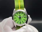 The P-A-R-T-Y? SJT Original wristwatch with a bright green dial and a green fabric strap featuring a yellow stripe, held by a white gloved hand against a dark background.