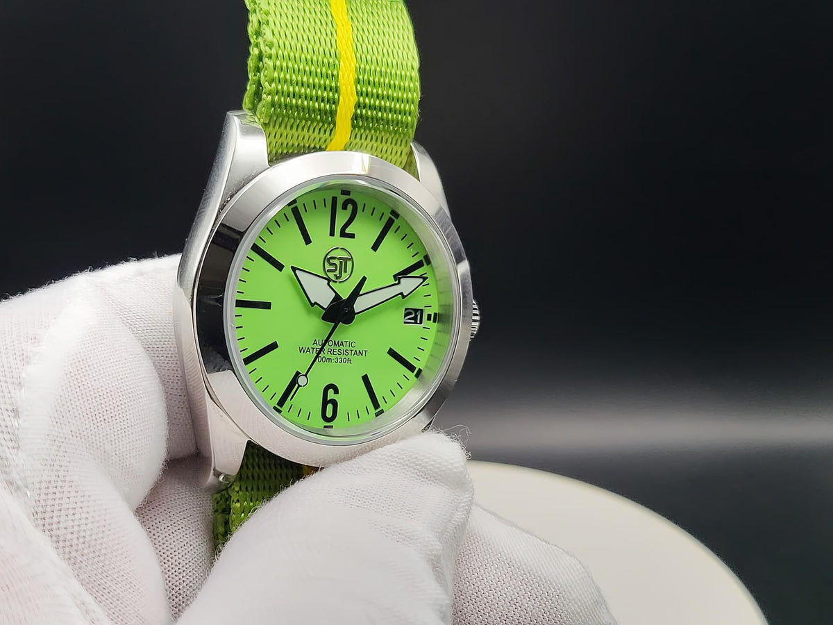 A close-up of The P-A-R-T-Y? SJT Original wristwatch with a bright green dial and matching green fabric strap held by a white gloved hand against a dark studio background.