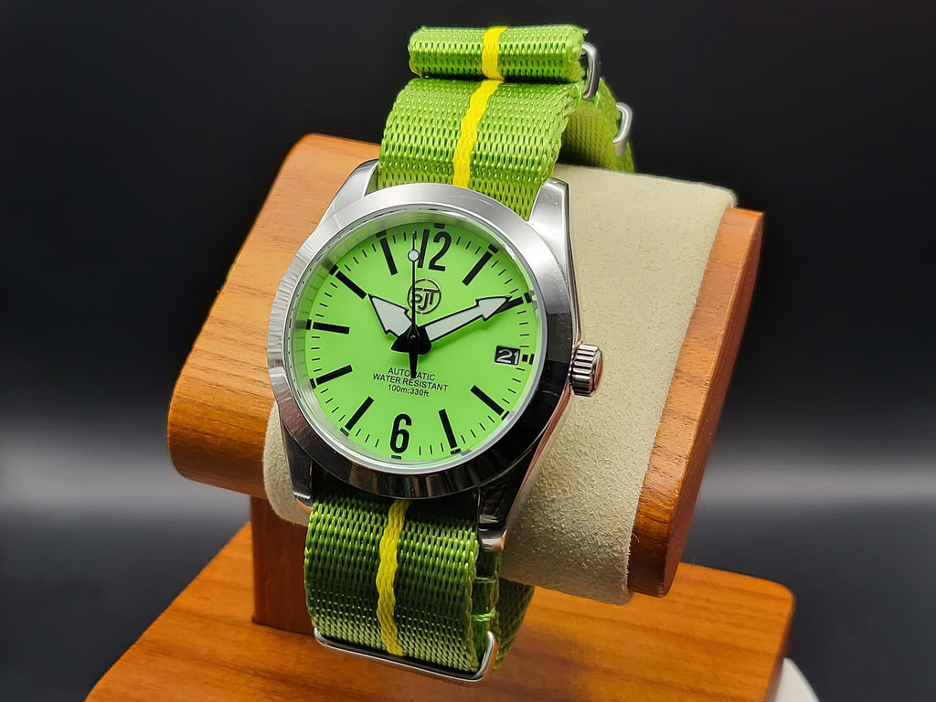 The P-A-R-T-Y? SJT Original wristwatch with a bright green dial, silver-toned metal case, and a green nylon strap with yellow stripes, displayed on a wooden stand against a dark background.