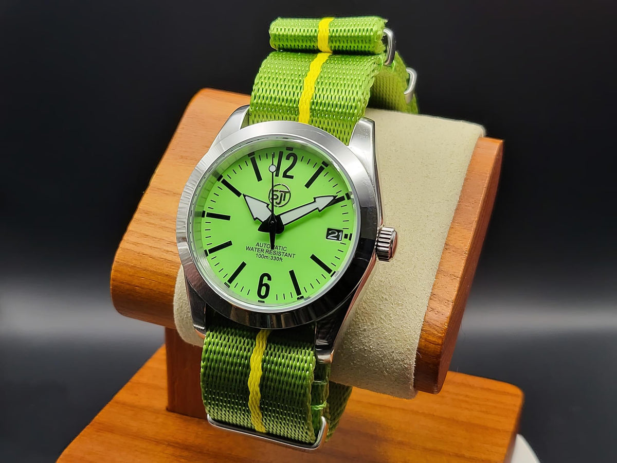 The P-A-R-T-Y? SJT Original wristwatch with a bright green dial, silver-toned metal case, and a green nylon strap with yellow stripes, displayed on a wooden stand against a dark background.