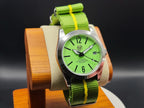 The P-A-R-T-Y? SJT Original wristwatch with a bright green dial and matching green fabric strap featuring yellow stripes, displayed on a wooden stand against a dark background.