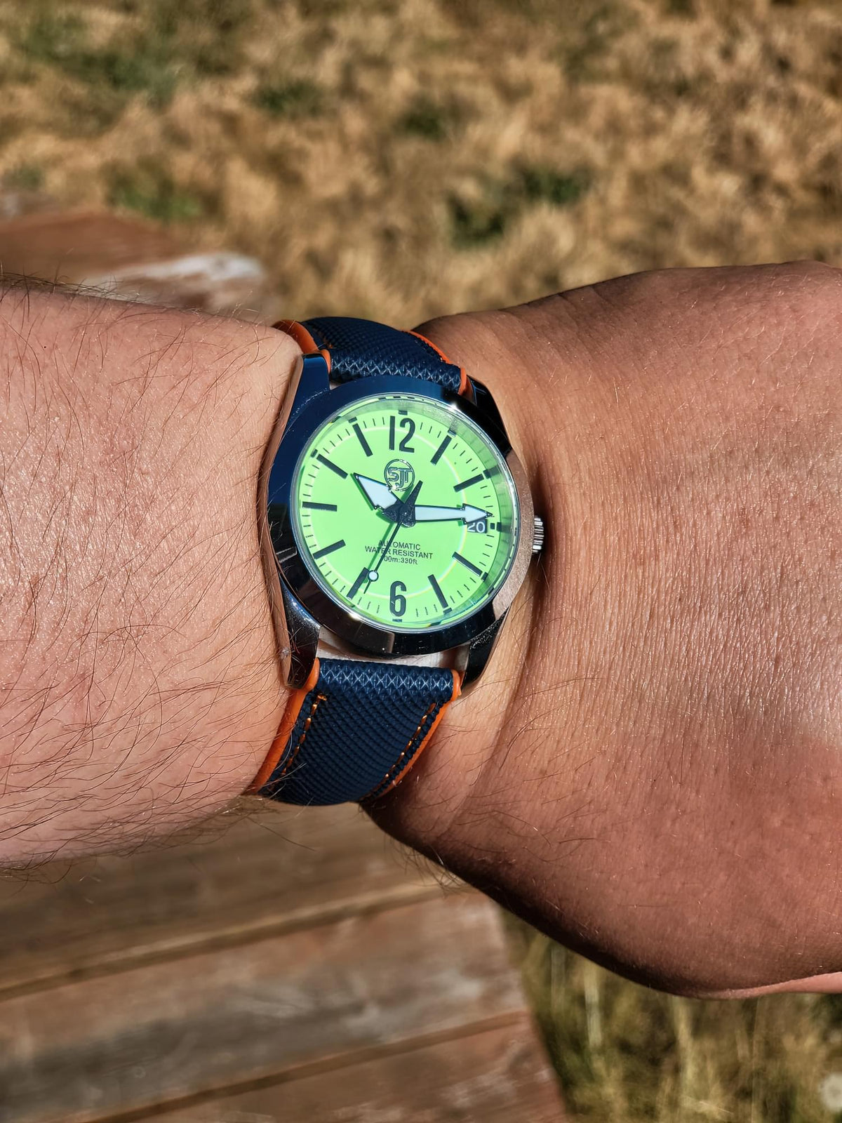 The P-A-R-T-Y? SJT Original wristwatch with a bright green dial and a dark blue textured strap with orange stitching, shown worn on a person's wrist outdoors.