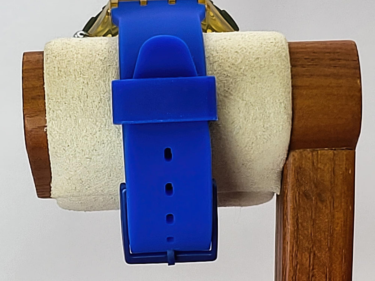 A bright blue silicone Swatch wristwatch strap attached to a gold-tone watch case, displayed on a white felt roll inside a wooden stand against a light gray background.