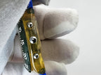 A close-up of a Swatch wristwatch wotj a transparent yellow watch band or strap with three silver metal rivets and a dark green inner strip showing white markings.