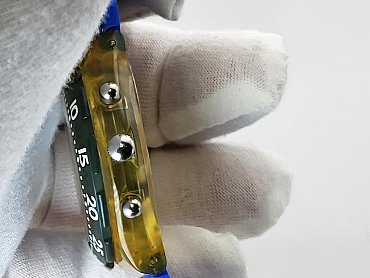A close-up of a Swatch wristwatch wotj a transparent yellow watch band or strap with three silver metal rivets and a dark green inner strip showing white markings.