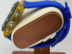 A close-up of a Swatch wristwatch with a translucent amber-yellow case and a blue silicone strap, mounted on a display stand against a light gray background.
