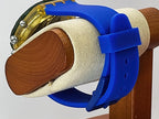 A close-up of a Swatch wristwatch with a blue silicone strap and a gold-toned transparent case, mounted on a wooden display stand with a beige foam sleeve.