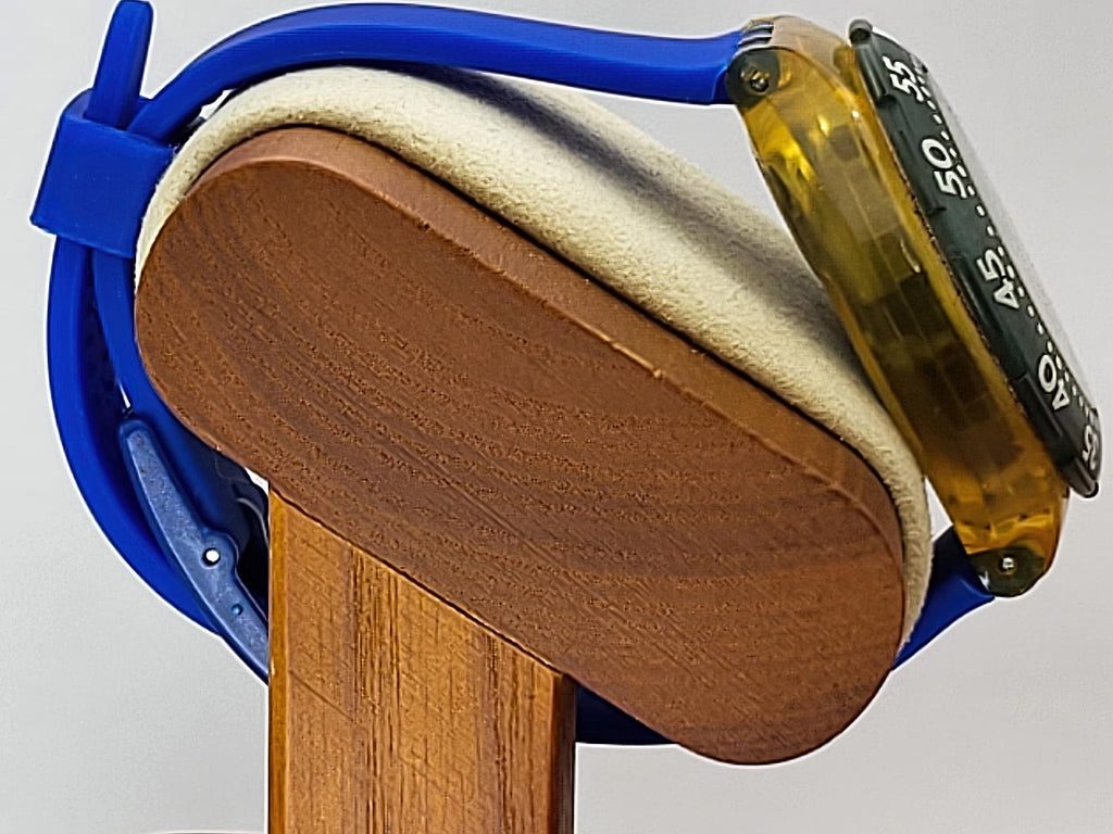 A close-up of a Swatch wristwatch with a translucent amber-yellow case, black bezel, and blue strap, resting on a wooden display stand.